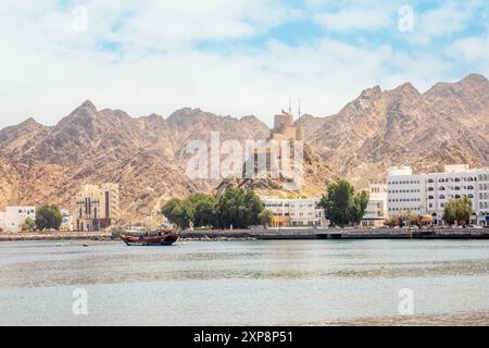 Promenade panoramique avec le château de Mutrah sur la colline et bateau traditionnel boutre ancré dans la baie, Muscat, sultanat Oman Banque D'Images