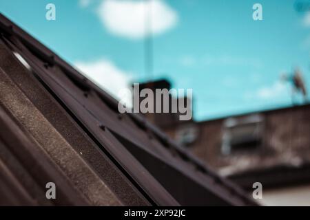 Couverture d'un bardeau de toit brun carrelé contre le ciel bleu. Construction de toiture en métal photo abstraite avec mise au point sélective. Logement, concept immobilier Banque D'Images