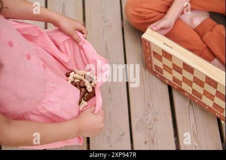 Vue en angle élevé d'enfants jouant aux échecs. Un enfant tenant des pièces d'échecs en robe rose tandis qu'un autre est assis avec échiquier sur plancher en bois. Banque D'Images
