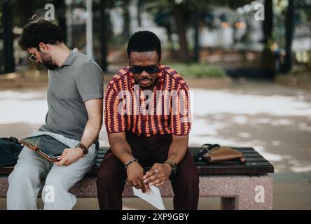Deux hommes assis sur un banc utilisant des appareils numériques dans un parc extérieur Banque D'Images