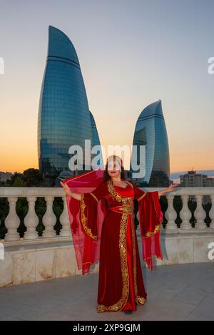Une belle fille en robe traditionnelle azerbaïdjanaise aux Flame Towers (2012) au coucher du soleil à Bakou, Azerbaïdjan Banque D'Images