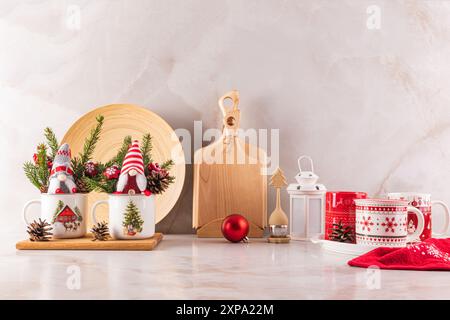 Deux gnomes du nouvel an dans des tasses et des branches d'épicéa sur le comptoir de cuisine avec des ustensiles écologiques en bois. Ambiance de Noël dans l'espace cuisine Banque D'Images