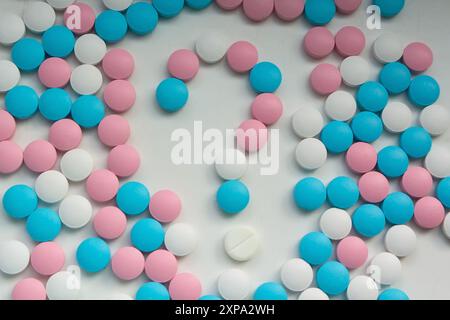 Des pilules blanches, bleues et roses en forme de point d'interrogation sont dispersées sur la table. Arrière-plan Banque D'Images