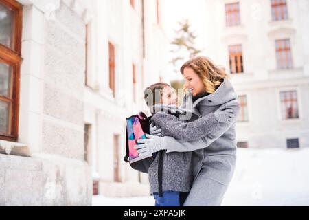 Mère emmenant sa fille à l'école, disant au revoir devant le bâtiment de l'école, se dirigeant vers le travail. Concept d'équilibre entre vie professionnelle et vie privée pour les femmes. Banque D'Images