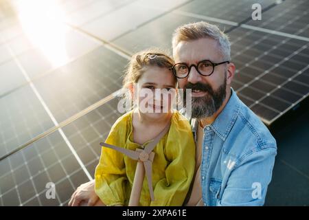 Fille et père sur le toit avec des panneaux solaires, tenant le modèle de l'éolienne. Installation solaire ou photovoltaïque sur le toit. Un avenir durable pour NEXT Banque D'Images