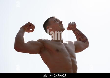 Homme musclé fléchissant les bras contre le ciel dégagé Banque D'Images