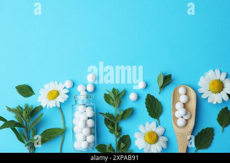 Homéopathie. Bouteille en verre, pilules, camomilles et feuilles vertes sur fond bleu clair, pose plate. Espace pour le texte Banque D'Images