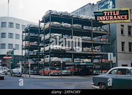 Un parking à ossature d'acier « Pigeon Hole », empilé plein d'automobiles dans le centre-ville de Portland, Oregon, États-Unis vers 1960. Il était situé à l'extrémité nord de SW Park Avenue. Le système de stationnement a été inventé par les frères Vaughn et Leo Sanders. Ils ont fondé Pigeon Hole parking en 1947. Ils ont breveté un ascenseur hydraulique ou ascenseur qui soulevait une voiture, la glissait dans une rangée et la poussait dans un espace dans le cadre. Le premier a eu lieu à Spokane, Washington, en 1950. D'autres ont suivi, mais lorsque les machines sont tombées en panne, les voitures ont été piégées pendant des jours. Pigeon Hole a cessé ses activités vers 1971 – une photographie vintage des années 1950/60. Banque D'Images