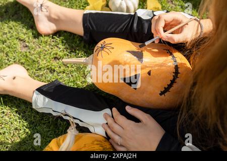 Enfant peint une grimace effrayante sur une citrouille d'Halloween avec de la peinture noire. Processus créatif, préparation pour Halloween. Joies et animations pour enfants. Banque D'Images