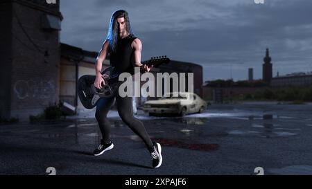 une rock star masculine se tient dans un environnement nocturne perdu et joue de sa guitare électrique. Banque D'Images