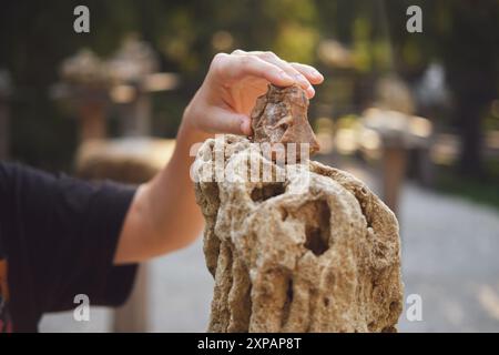 Placer à la main une petite roche brune sur une grande pierre poreuse dans un cadre extérieur. Nature et concept d'activité de plein air pour le design et l'impression. Banque D'Images