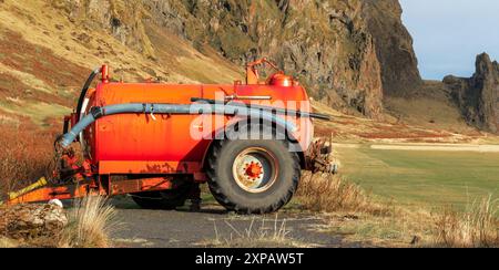 Un tracteur orange est stationné dans un champ avec une montagne en arrière-plan. Le tracteur est vieux et rouillé, et il est abandonné. La scène a un sens de Banque D'Images