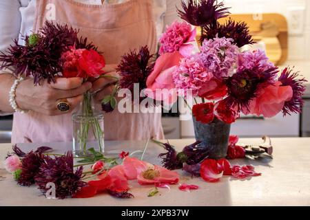 Femme arrangeant un bouquet de coquelicots dans un vase sur un comptoir de cuisine Banque D'Images