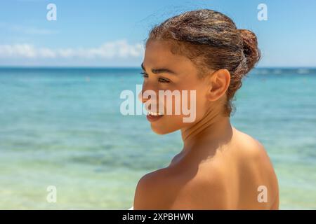 Une femme magnifique dans un bikini blanc pose sur une plage immaculée, entourée d'eaux cristallines. Sa beauté et le cadre tropical créent une image Banque D'Images