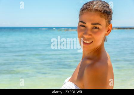 Une beauté ensoleillée se prélasse dans la lueur chaude du paradis. Vêtue d'un bikini blanc immaculé, son sourire éclatant illumine la plage tropicale. Banque D'Images