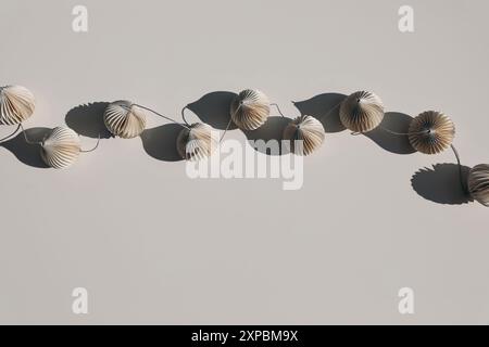 Guirlande élégante de boules de noël en papier sur fond de table beige à la lumière du soleil, de longues ombres. Décoration festive scandinave bohème minimale Banque D'Images