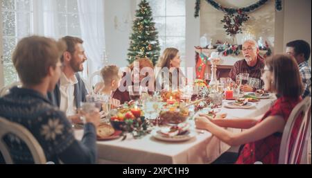 Les membres de la famille multigénérationnelle partagent des histoires drôles et de la joie lors d'un dîner de dinde de Noël. La maison est remplie de l'esprit de vacances de la saison d'hiver que les parents et les proches apprécient un repas de fête Banque D'Images