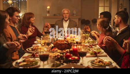 Famille religieuse célébrant Noël à la maison. Parents et amis priant et se tenant la main, bénissant la nourriture avant de manger le dîner. Chrétiens remerciant Dieu pour avoir fourni un délicieux rôti de dinde Banque D'Images