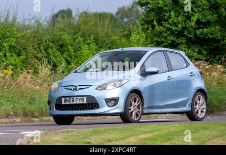 Whittlebury, Norhants, Royaume-Uni - 4 août 2024. 2008 voiture bleue Mazda 2 conduisant sur une route de campagne britannique Banque D'Images