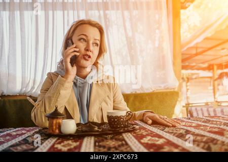 Femme parlant au téléphone à un café avec une tasse de café turc Banque D'Images