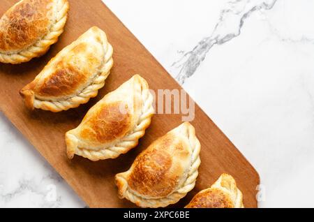 Empanadas de bœuf argentin typiques sur une planche de bois sur fond de marbre blanc. Banque D'Images