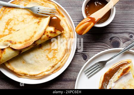 Crêpes argentines remplies de dulce de leche dans des plaques blanches sur fond de bois. Banque D'Images