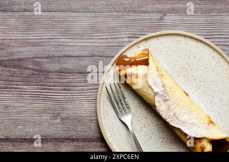 Crêpe Argentine remplie de dulce de leche et de sucre glace sur le dessus dans une plaque beige sur fond de bois avec espace de copie. Banque D'Images