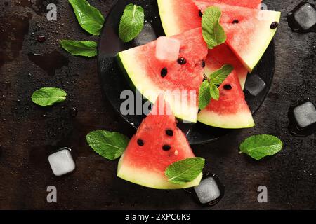 Tranches de pastèque mûre juteuse sur une plaque noire sur un fond sombre avec de la menthe et des glaçons. Vue de dessus. Un fruit d'été rafraîchissant. Ingrédients Banque D'Images