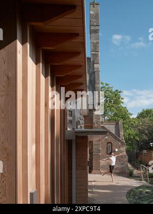 Détail de la façade en bois et danseuse exerçant à l'extérieur. Rambert School of Ballet, Londres, Royaume-Uni. Architecte : MICA, 2023. Banque D'Images