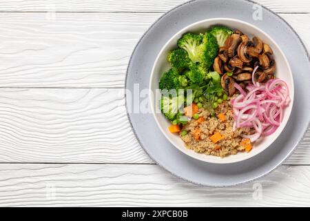 quinoa à la patate douce, champignons sautés, oignon rouge mariné, pois verts, brocoli bouilli dans un bol blanc sur une table en bois blanc, déjeuner végétalien, horizont Banque D'Images