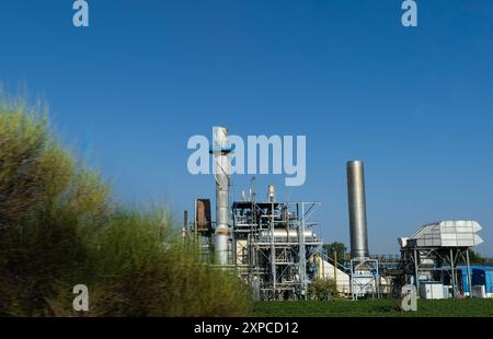 Vue extérieure d'une papeterie industrielle entourée de plantes vertes. Il a deux cheminées. Écologie, net zéro et pollution atmosphérique avec serres Banque D'Images