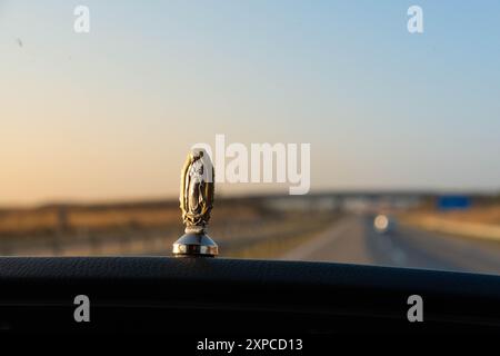 Une figurine de la Vierge de Guadalupe collée sur le tableau de bord d'une voiture. En arrière-plan, une autoroute floue avec un grand pont. Christianisme, p Banque D'Images