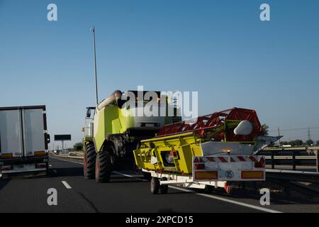 Une énorme moissonneuse-batteuse se déplace lentement sur une autoroute et est dépassée par un camion de chargement. La machine se déplace sur la voie de droite pour éviter les obstacles Banque D'Images