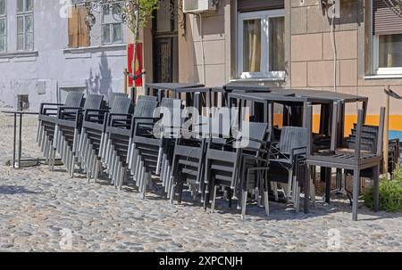 Piles de chaises et de tables en rotin noir devant le café de Cobbled Street Banque D'Images