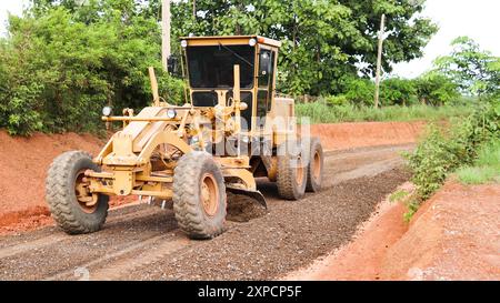 Niveleuse nivelant les graviers sur un chemin de terre en préparation pour le revêtement d'asphalte en vue de la construction de nouvelles routes. Parfait pour illustrer les professionnels de la construction de routes Banque D'Images