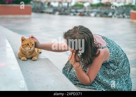 Mignonne adolescente caresse un chat gingembre sans abri dans la rue Banque D'Images