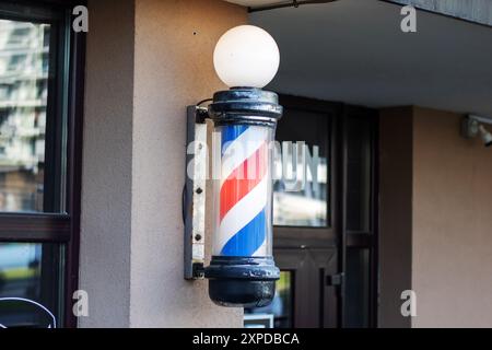 Un poteau de barbier rouge, blanc et bleu est monté sur le mur extérieur d'un bâtiment, servant d'accessoire traditionnel pour le salon de coiffure Banque D'Images