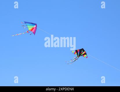 deux grands cerfs-volants colorés avec des couleurs arc-en-ciel volant dans le ciel bleu attaché à une ficelle Banque D'Images