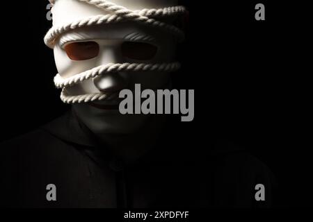 Représentation théâtrale. Homme avec masque en plastique et corde de chanvre sur fond noir, espace pour le texte Banque D'Images