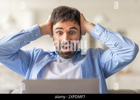 Homme choqué réagissant à l'écran de l'ordinateur portable tout en étant assis à l'intérieur Banque D'Images