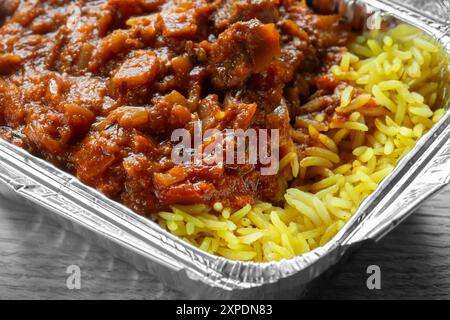 Agneau Rogan Josh curry indien avec riz pilau repas à emporter dans un emballage de plateau en aluminium. Sur fond de planche de bois Banque D'Images
