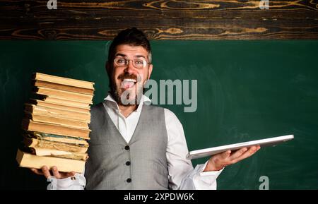 Professeur heureux avec ordinateur portable et manuel en classe. Choix entre la technologie éducative moderne ou la méthode traditionnelle. Éducation moderne. Smiling stu Banque D'Images