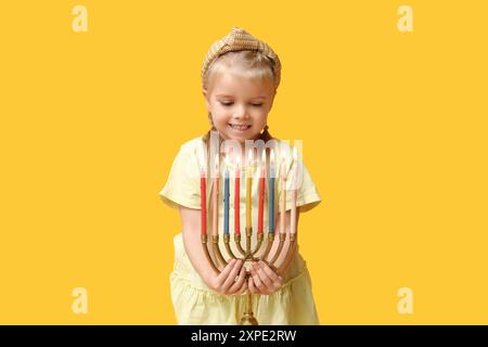 Jolie petite fille heureuse avec menorah sur fond jaune. Célébration Hanukkah Banque D'Images