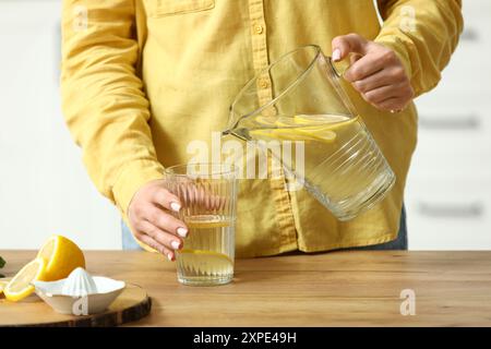 Jeune femme versant de l'eau infusée au citron de la cruche dans le verre dans la cuisine Banque D'Images