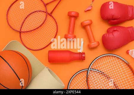 Équipement de sport avec haltères et raquettes sur fond orange. Vue de dessus Banque D'Images