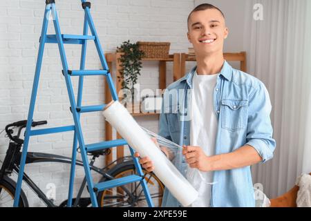 Jeune homme avec rouleau de film étirable à la maison Banque D'Images