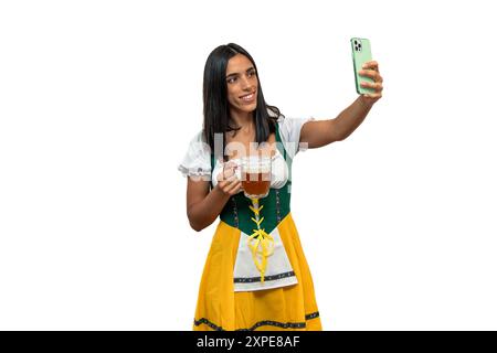 une fille bavaroise vêtue de vêtements traditionnels oktoberfest prend un selfie avec son smartphone. L'image capture l'esprit festif et le tradi culturel Banque D'Images