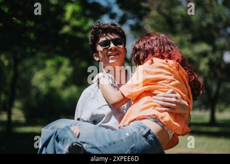 Jeune homme portant la femme dans le parc par une journée ensoleillée, exprimant l'amour et la joie Banque D'Images