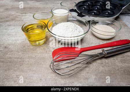 Un fouet rouge et argent est sur une table avec d'autres articles de cuisine. Le fouet est entouré de bols de farine, de sucre et d'autres ingrédients Banque D'Images