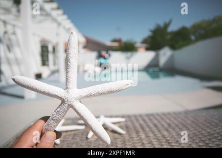 Une vue d'une main tenant une étoile de mer blanche, une piscine arrière-cour. Banque D'Images